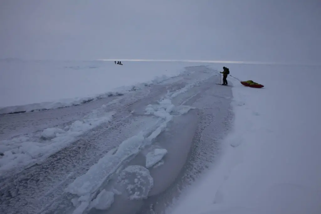 Skier crossing partially frozen open lead at North Pole.